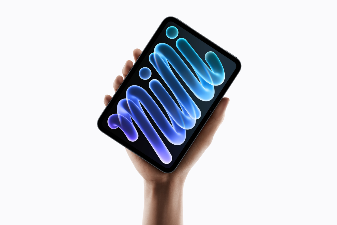 Mão segurando o iPad mini na vertical sobre fundo claro, com a palavra mini estilizada em azul e roxo na tela.