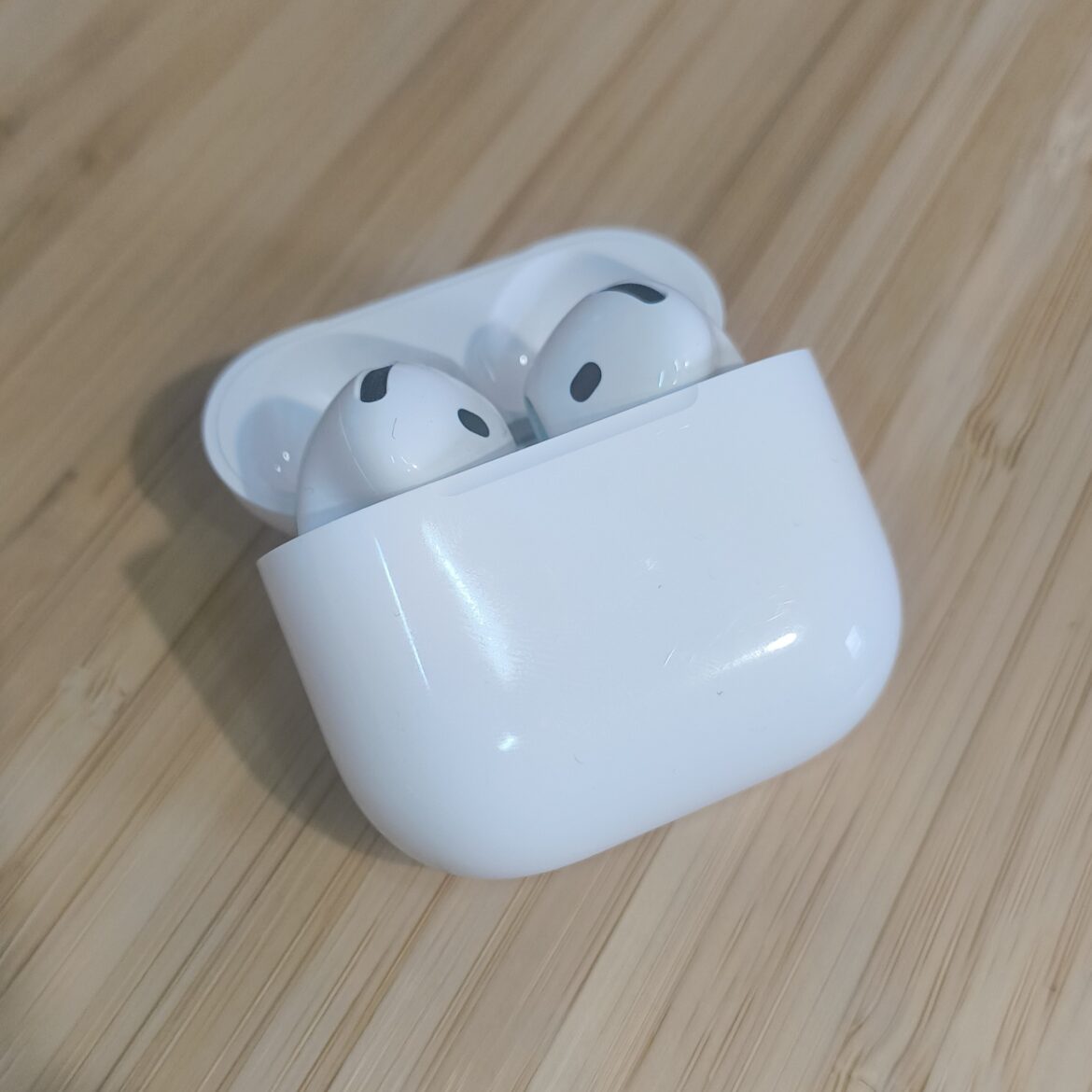 AirPods 5 em um estojo de recarga aberto sobre uma mesa de madeira.